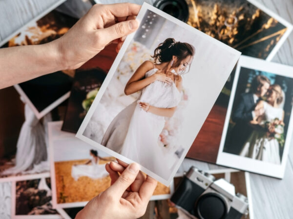Printed wedding photos with the bride and groom, a vintage black camera and woman hands with photo